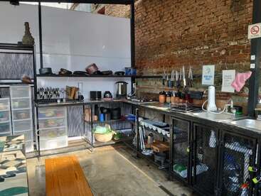 Cette image montre une cuisine rustique et organisée avec des étagères ouvertes, des ustensiles, de la vaisselle, un double évier, des murs en briques, des tiroirs en plastique et une variété d'ustensiles de cuisine bien rangés.