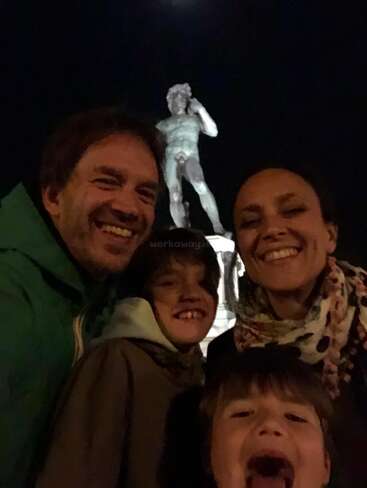 A smiling family of four takes a nighttime selfie in front of a large, illuminated statue, capturing their joy and excitement during their outing together.