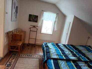 Dieses gemütliche Schlafzimmer hat ein großes Bett mit einer blau gestreiften Bettdecke, Holzmöbel, einen dekorativen Teppich, Wandkunst, einen kleinen Schreibtisch und ein Fenster mit Vorhängen.