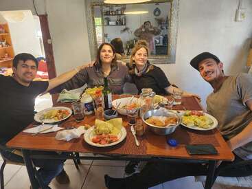 Quatre personnes sont joyeusement assises autour d'une table à manger pour prendre un repas ensemble, avec des assiettes de nourriture, des salades, des boissons et une atmosphère chaleureuse et familiale en arrière-plan.