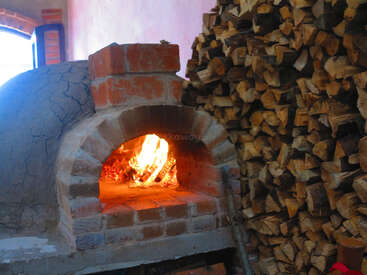A traditional brick wood-fired oven burns brightly with stacked firewood beside it, creating a warm, rustic atmosphere. Perfect for baking bread or pizza.
