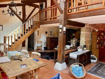 Essa aconchegante sala de estar rústica apresenta vigas de madeira expostas, uma escada de madeira, área de loft, piso de terracota, móveis vintage, uma mesa de jantar e uma encantadora decoração eclética.