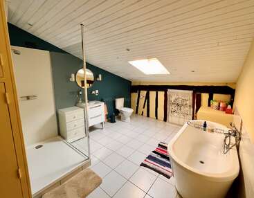 Esse espaçoso banheiro no sótão tem banheira, chuveiro, vaso sanitário, pia com espelho redondo, claraboia, piso de azulejos, teto inclinado e toques decorativos aconchegantes.