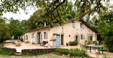 Esta encantadora casa de campo apresenta paredes amarelas claras e persianas azuis. Cercada por vegetação, ela tem um pátio espaçoso com assentos ao ar livre, mesas e um ambiente descontraído.