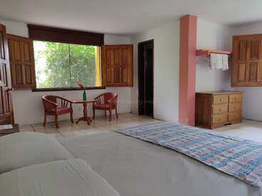 L'image représente une pièce sereine avec des murs blancs, une grande fenêtre et un lit, avec des meubles en bois et un tapis vibrant, dégageant un sentiment de calme et de tranquillité.