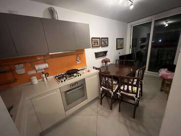 Diese gemütliche Küche hat moderne Schränke, eine orangefarbene Aufkantung, einen Gasherd, einen Esstisch aus Holz mit sechs Stühlen, Wandkunst, Blumen und eine große Glastür.