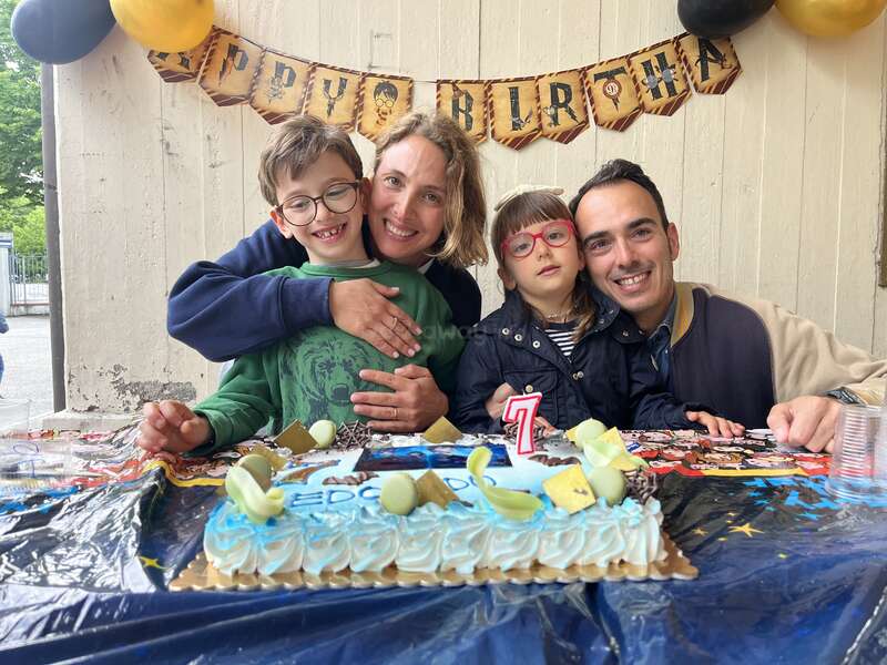 Eine fröhliche Familie feiert den 7. Geburtstag eines Kindes mit einer Torte. Dekorationen und Luftballons sorgen für eine festliche Atmosphäre. Alle lächeln und genießen diesen besonderen Moment zusammen.
