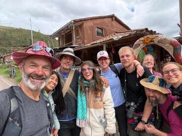 Un groupe de personnes joyeuses posent pour un selfie devant un bâtiment rustique, vêtues de chapeaux et de vêtements d'extérieur, profitant ensemble de leur aventure sous un ciel nuageux.