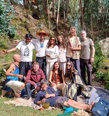 Un groupe de douze personnes pose en plein air sur une pelouse, souriant joyeusement. Elles sont entourées d'arbres, de couvertures et de soleil, profitant d'un moment de détente ensemble.