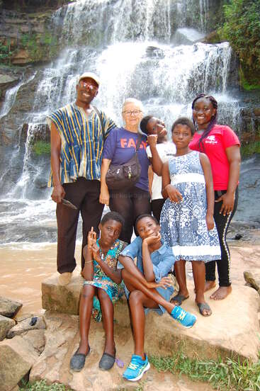Eine Gruppe von sieben Personen, darunter Erwachsene und Kinder, posiert fröhlich vor einem wunderschönen Wasserfall und genießt gemeinsam ein malerisches Abenteuer in der Natur.