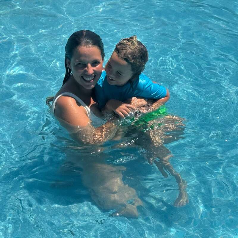 Una mujer y un niño sonríen y se divierten juntos en una piscina de aguas cristalinas, creando un momento veraniego alegre y reconfortante.