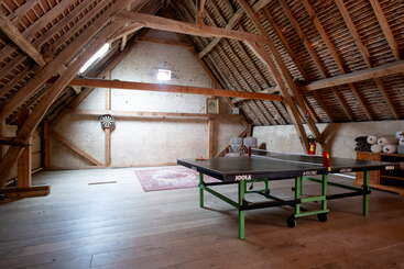 Dieses gemütliche Dachzimmer besticht durch Holzbalken, eine Tischtennisplatte, eine Dartscheibe, einen Orientteppich, viel Tageslicht, aufgerollte Matten und eine gemütliche, rustikale Atmosphäre.