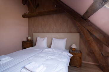 Dieses gemütliche Schlafzimmer verfügt über ein Doppelbett mit frischer weißer Bettwäsche, zwei Nachttische aus Holz, sanfte Beleuchtung, freiliegende Holzbalken und schräge Decken, die ihm einen rustikalen Charme verleihen.