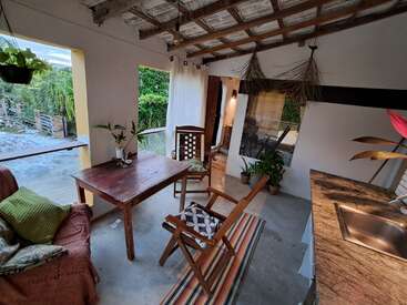 Este quarto aconchegante e ao ar livre apresenta móveis rústicos de madeira, plantas verdes, galhos decorativos pendurados, uma pia de cozinha, luz natural, um sofá confortável e vista para o jardim ao ar livre.