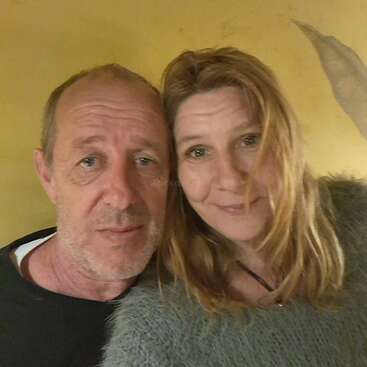 Um homem e uma mulher estão tirando uma selfie em close-up juntos. Ambos têm cabelos claros e estão sorrindo gentilmente, com um fundo amarelo atrás deles.
