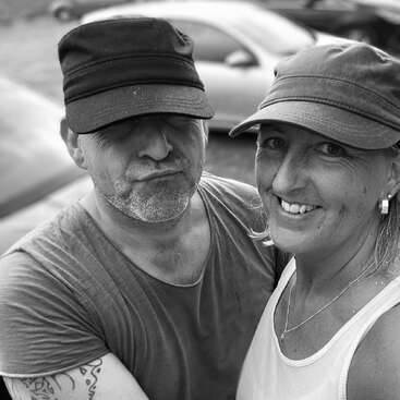 Une photo en noir et blanc montre deux personnes portant des casquettes et des vêtements décontractés, souriant et posant ensemble en plein air. Elles semblent heureuses et à l'aise l'une avec l'autre.