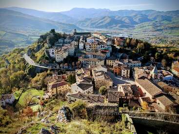 Un village pittoresque situé au sommet d'une colline, avec un ensemble de maisons colorées, des routes sinueuses, entouré de collines et de montagnes verdoyantes sous un ciel bleu clair, rayonnant de charme.
