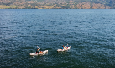 Deux personnes font du kayak sur un immense lac paisible, entouré de montagnes. L'eau bleue reflète le ciel, créant un cadre paisible et pittoresque propice à l'aventure en plein air.