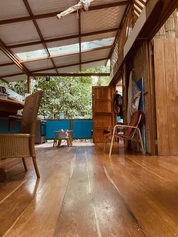 Este acogedor interior de madera presenta puertas abiertas, luz natural, muebles rústicos y exuberantes vistas verdes al exterior, combinando el confort interior con un ambiente de bosque sereno y acogedor.