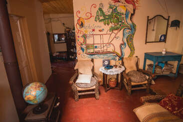 Sala colorida e aconchegante com cadeiras rústicas, um mapa mural pintado de Pichilemu, móveis de madeira, um globo terrestre e várias decorações, criando uma atmosfera calorosa e convidativa.