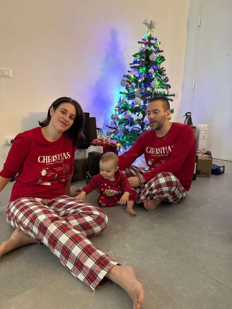 A family of three, dressed in matching Christmas pajamas, sits by a decorated tree with presents. The atmosphere is festive and joyful, celebrating Christmas together.
