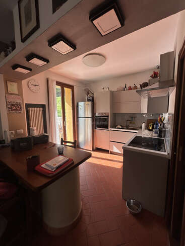 Esta é uma cozinha moderna e aconchegante com luz natural, piso de terracota, eletrodomésticos de aço inoxidável, uma mesa de madeira, relógio de parede, itens de decoração e uma tigela para animais de estimação.