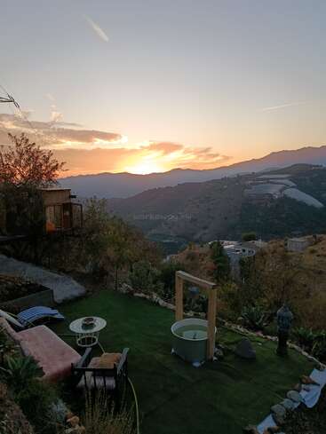 A beautiful sunset over rolling hills, with a cozy outdoor seating area, artificial grass, garden decorations, and a tranquil, peaceful atmosphere in the countryside.