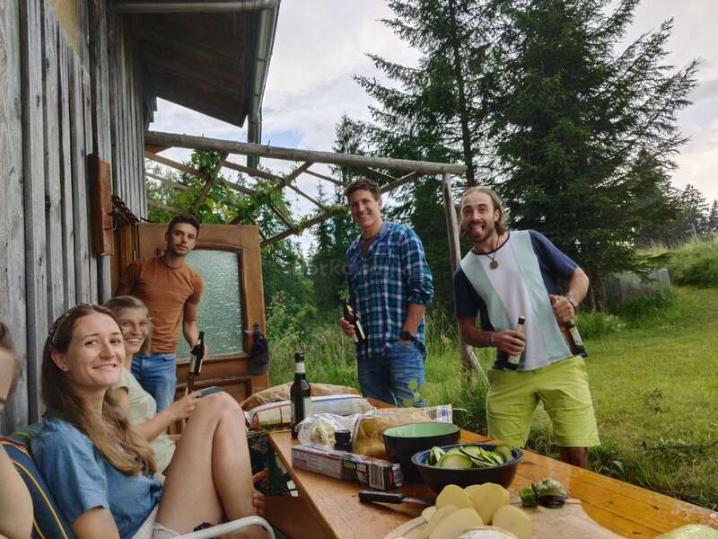 La imagen muestra a un grupo de cinco personas reunidas en torno a una mesa de madera, rodeadas de un sereno entorno al aire libre con árboles y césped.