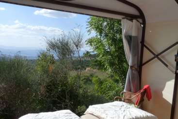 The image depicts a serene outdoor setting, featuring a bed with a white comforter and a red towel, set against a picturesque landscape with trees and a distant mountain range.
