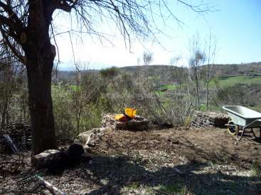 The image depicts a rural landscape with a tree, wheelbarrow, and gardening tools, set against a backdrop of rolling hills and a clear blue sky.