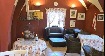 This cozy room features red arched walls, floral tablecloths, wicker chairs, framed pictures, a small window, and soft lighting, creating a warm and inviting atmosphere.