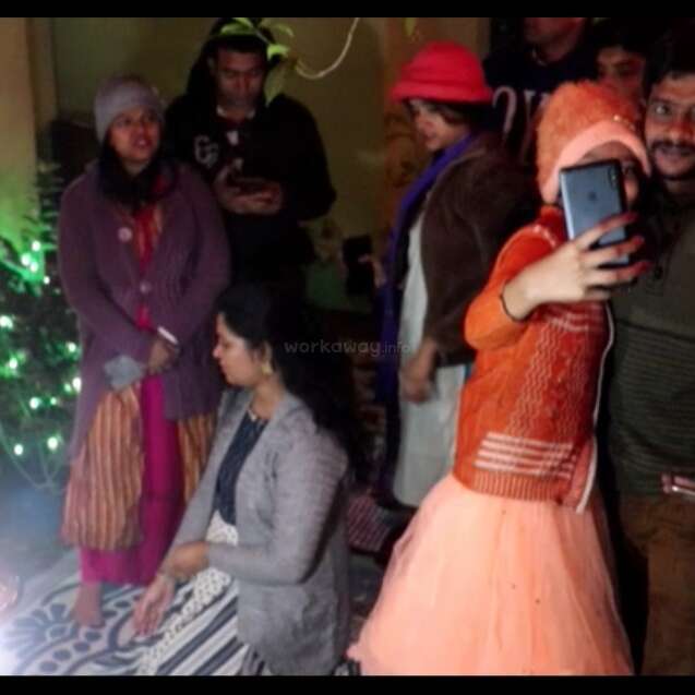 The image depicts a group of people gathered around a table, engaged in a lively discussion, with some individuals gesturing and others listening intently, conveying a sense of engagement and interaction.