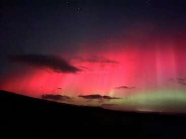 The image depicts a breathtaking night sky with a vibrant red and green aurora borealis, set against a dark landscape with a few clouds and stars twinkling above.