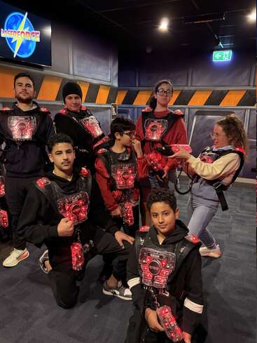 Un grupo de niños y adolescentes con chalecos de láser tag posan en una pista cubierta de láser tag. Parecen entusiasmados y listos para jugar.