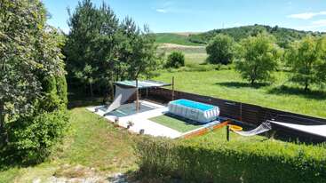 Ce jardin serein comprend une piscine hors sol surélevée, deux hamacs, un coin salon ombragé, une pelouse verdoyante, des arbres environnants et de magnifiques collines en arrière-plan.
