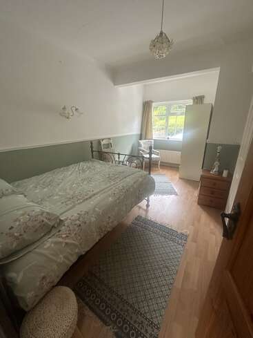 Une chambre à coucher confortable comprend un lit simple avec des draps à fleurs, des meubles en bois, une fenêtre avec des rideaux, deux chaises, des tapis à motifs et un plafonnier décoratif.