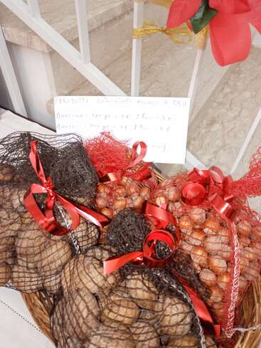 Bolsas de nueces y avellanas en sacos de malla atados con cintas rojas. Al fondo se ve un cartel con el precio escrito a mano y adornos festivos.