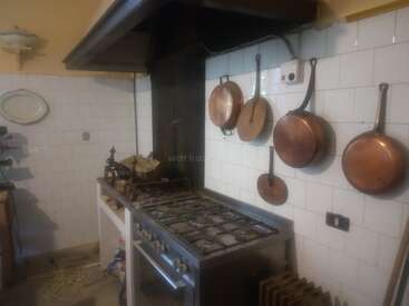 Esta imagen muestra una cocina de época con una gran cocina de gas, sartenes de cobre antiguas colgadas de paredes alicatadas y una decoración rústica, que evoca un ambiente acogedor y tradicional.