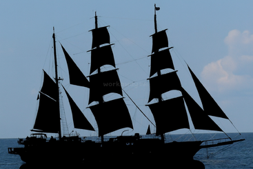 Die dramatische Silhouette eines klassischen Großseglers mit ausgebreiteten Segeln, der majestätisch auf dem offenen Meer unter einem heiteren Himmel treibt, erinnert an abenteuerliche Reisen.