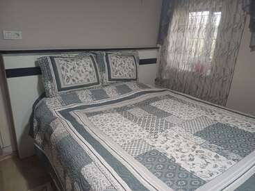 Un lit soigneusement fait avec un édredon à motifs et deux oreillers assortis se trouve à côté d'une fenêtre aux rideaux diaphanes et décoratifs dans une chambre à coucher douillette et doucement éclairée.