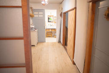 Un couloir lumineux et épuré, doté d'un parquet, mène à une salle de bains confortable. Un éclairage tamisé, une décoration épurée et un mobilier simple créent un intérieur chaleureux et accueillant d'inspiration japonaise.
