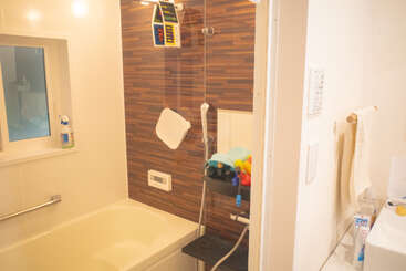 Une salle de bains épurée et moderne, équipée d'une baignoire, d'un espace douche, d'un mur au motif bois, d'articles de toilette, d'une fenêtre, d'un porte-serviettes, d'un miroir et de divers jouets de bain disposés sur une étagère.