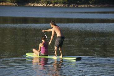 The image depicts a man and woman on a paddleboard in a body of water, with the man standing and the woman sitting.
