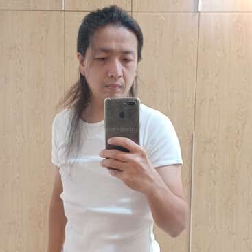 L'image montre une personne prenant un selfie devant un miroir, portant un t-shirt blanc et tenant un téléphone avec un étui gris.