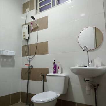 Il s'agit d'une salle de bain propre équipée d'un WC, d'un lavabo, d'un miroir rond, d'une douche avec chauffe-eau, de savon, de shampoing, d'un porte-savon, d'un gobelet et d'une petite fenêtre.