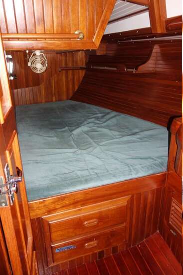 Das Bild zeigt eine kompakte Holzhütte mit einem Einzelbett, einer grünen Matratze, Schubladen und einem Ventilator, die einen gemütlichen und funktionalen Raum darstellen.