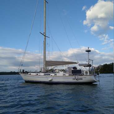 Das Bild zeigt ein weißes Segelboot mit dem Namen \"TE ARAWA\" an der Seite, das auf einem Gewässer unter einem blauen Himmel mit Wolken treibt.