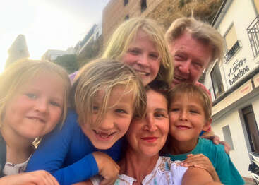 Une famille heureuse de six personnes sourit lors d'un selfie de groupe en plein air avec des bâtiments en arrière-plan. Tout le monde a l'air joyeux, profitant d'une sortie ensoleillée ensemble.