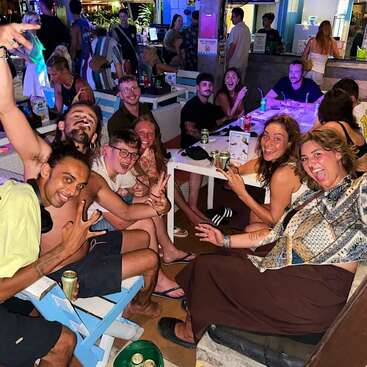 A lively group of friends enjoys a night out at a vibrant bar, smiling, posing enthusiastically, holding drinks, and soaking in the fun, energetic atmosphere.