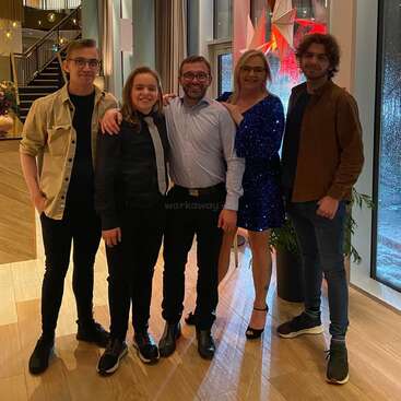 La imagen muestra a cinco personas de pie en una habitación bien iluminada con una escalera, posando para una foto, en un ambiente de camaradería y alegría.
